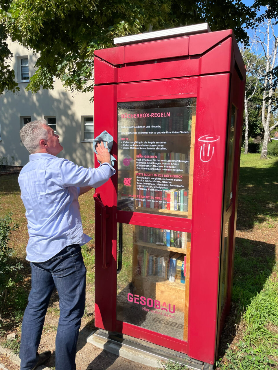 Christian Wilkens, Vorstand der GESOBAU, reinigt eine rote Bücherbox in Borsigwalde