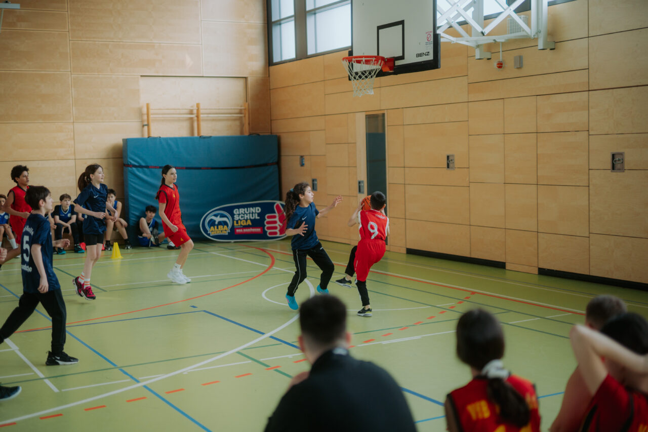 Schulkinder spielen Basketball in einer Sporthalle